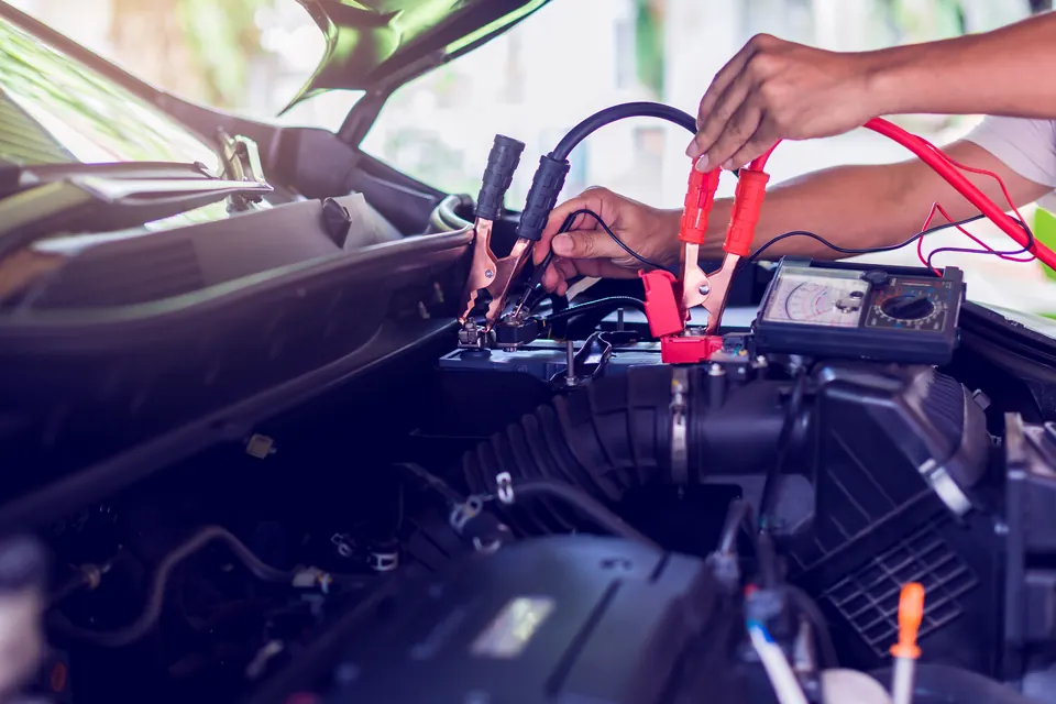 A technician testing a car battery with a meter and clamps