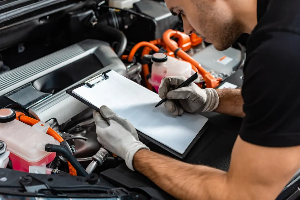 A technician writing on a clipboard while inspecting an engine bay
