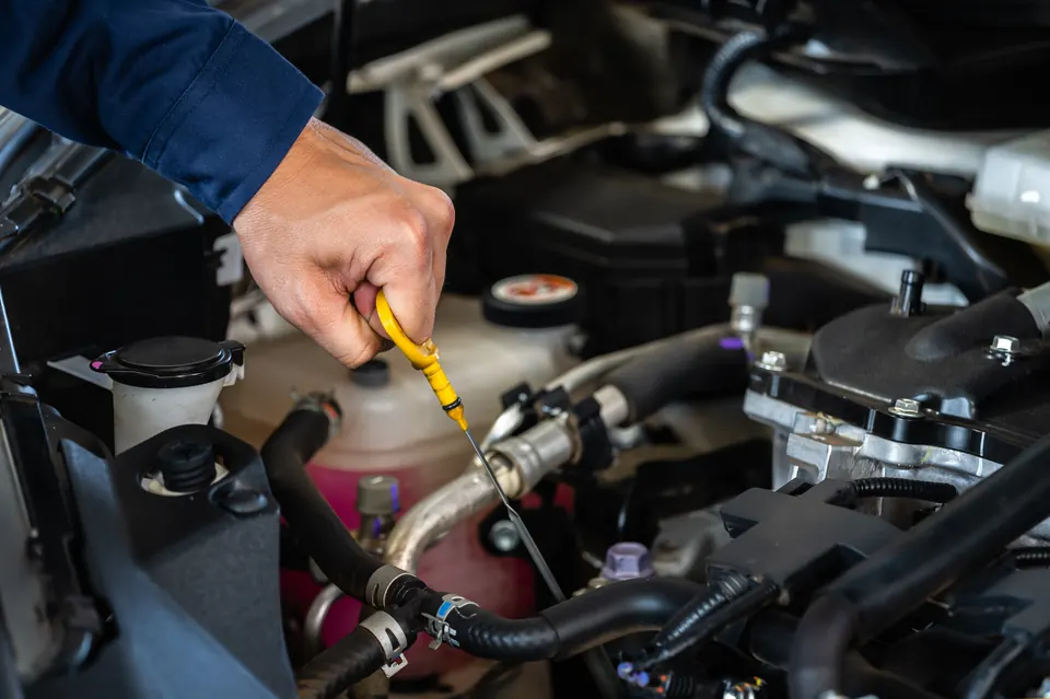 A technician's hand pulling the yellow oil dipstick in an engine bay