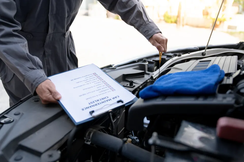 A technician holding a maintenance checklist while pulling the oil dipstick