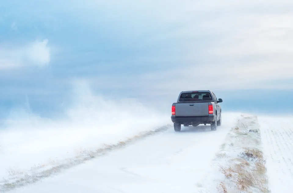 A pickup truck driving a snowy road in blowing wind