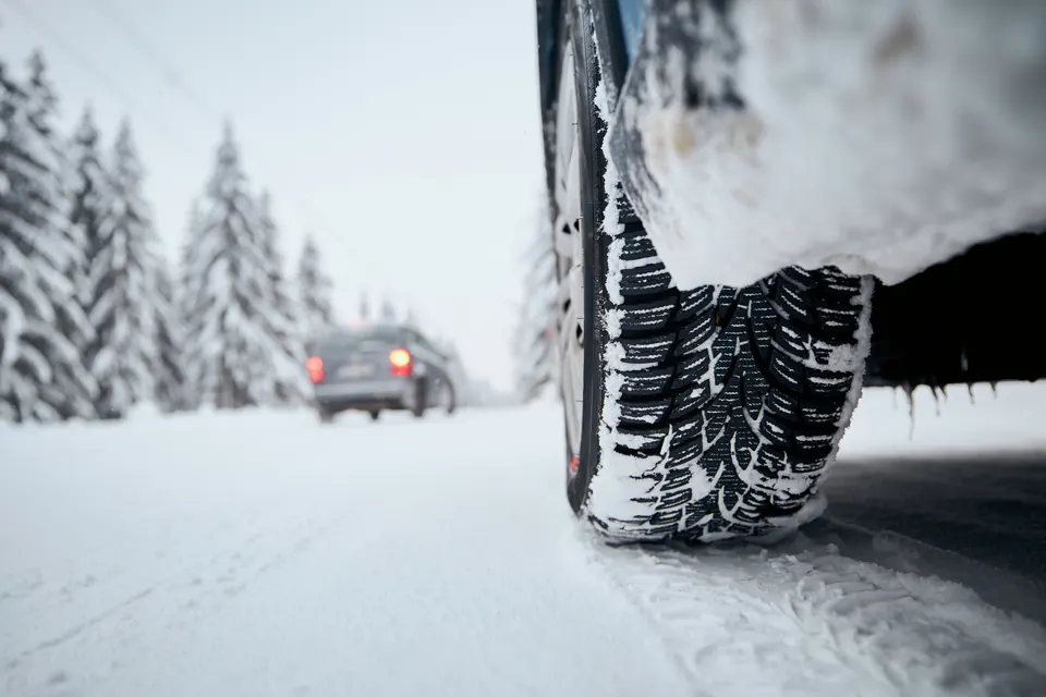 A car tire on a snow-covered road with a car driving behind it