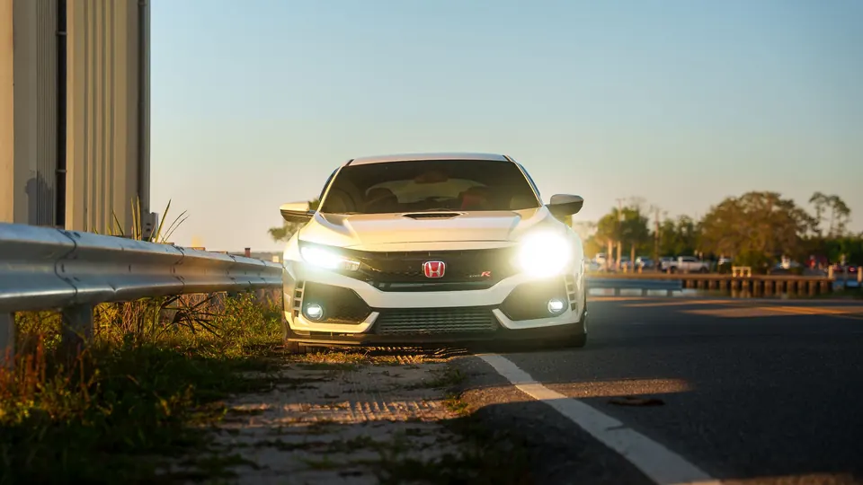 A car with its headlights on beside a highway at dusk